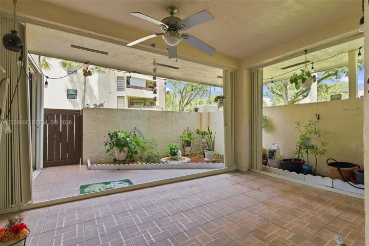Private paver patio with ceiling fan, screened enclosure, and a planted garden bed along the perimeter wall.