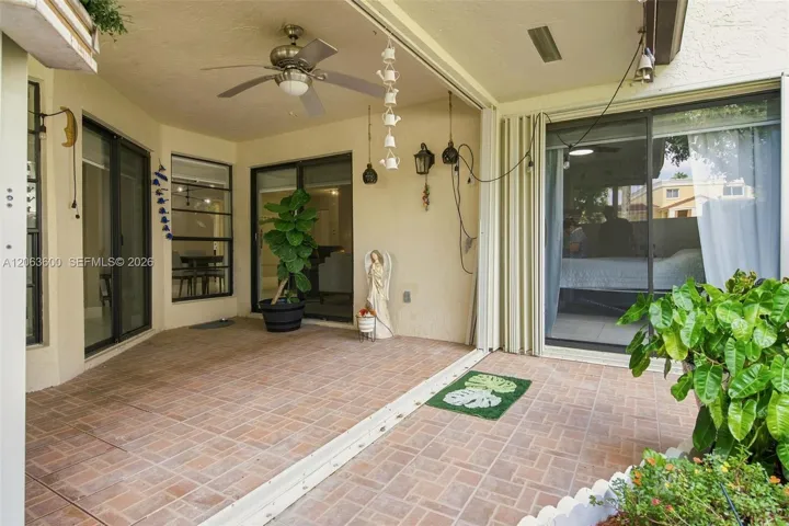 Private paver patio with ceiling fan, sliding glass door access to the living room and primary bedroom, and potted greenery throughou