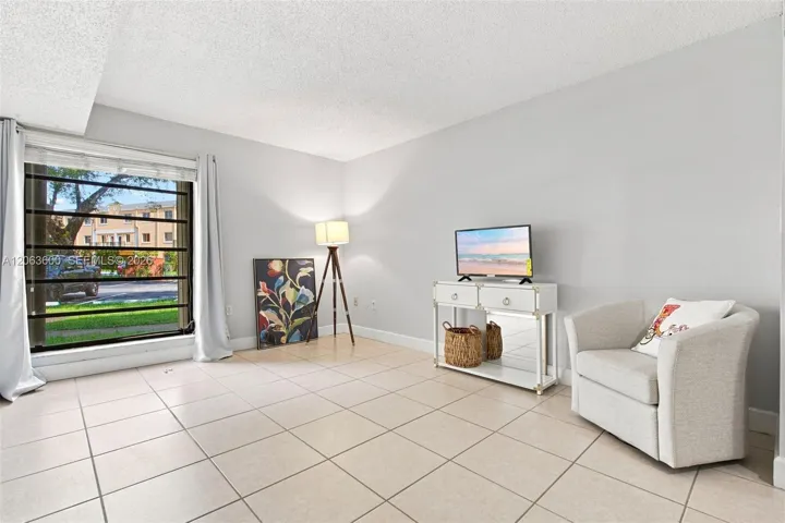 Bedroom with tile flooring, large window with security bars and natural light, and neutral wall color.
