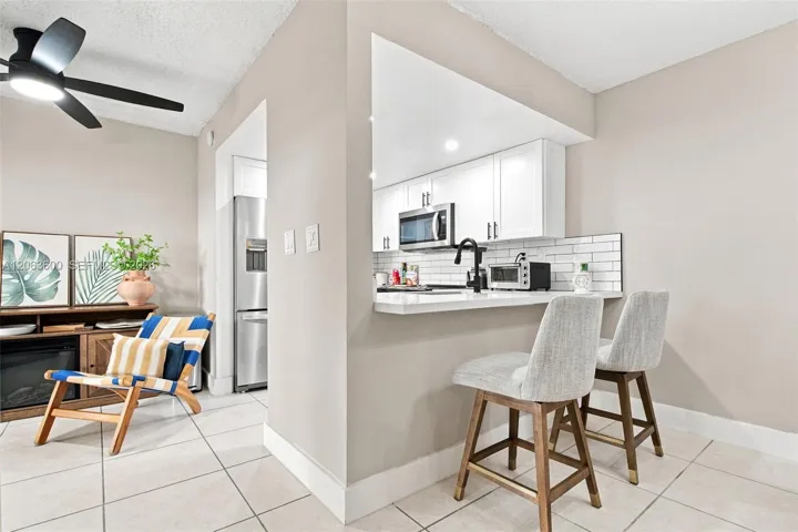 Pass-through kitchen with white cabinetry, subway tile backsplash, stainless steel microwave, and breakfast bar seating for two.