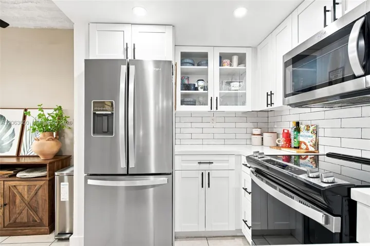 Remodeled kitchen with white shaker cabinetry, quartz countertops, subway tile backsplash, stainless steel refrigerator, and glass-front upper cabinets.