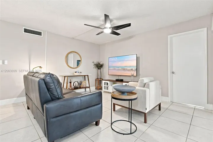 Living area with tile flooring, ceiling fan, and wall-mounted TV; door at right leads to the patio.