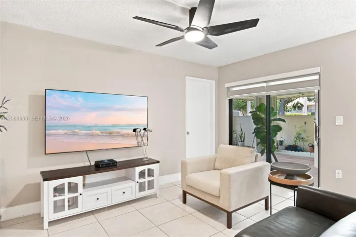 Living area with sliding glass doors to the private patio, ceiling fan, and neutral wall color throughout.