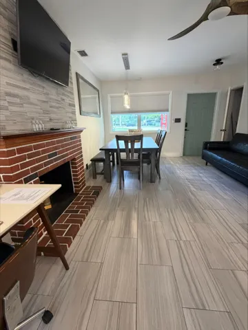 Wide tile wood like finish flooring extends into dining area with a modern ceiling fan and a brick-faced fireplace.