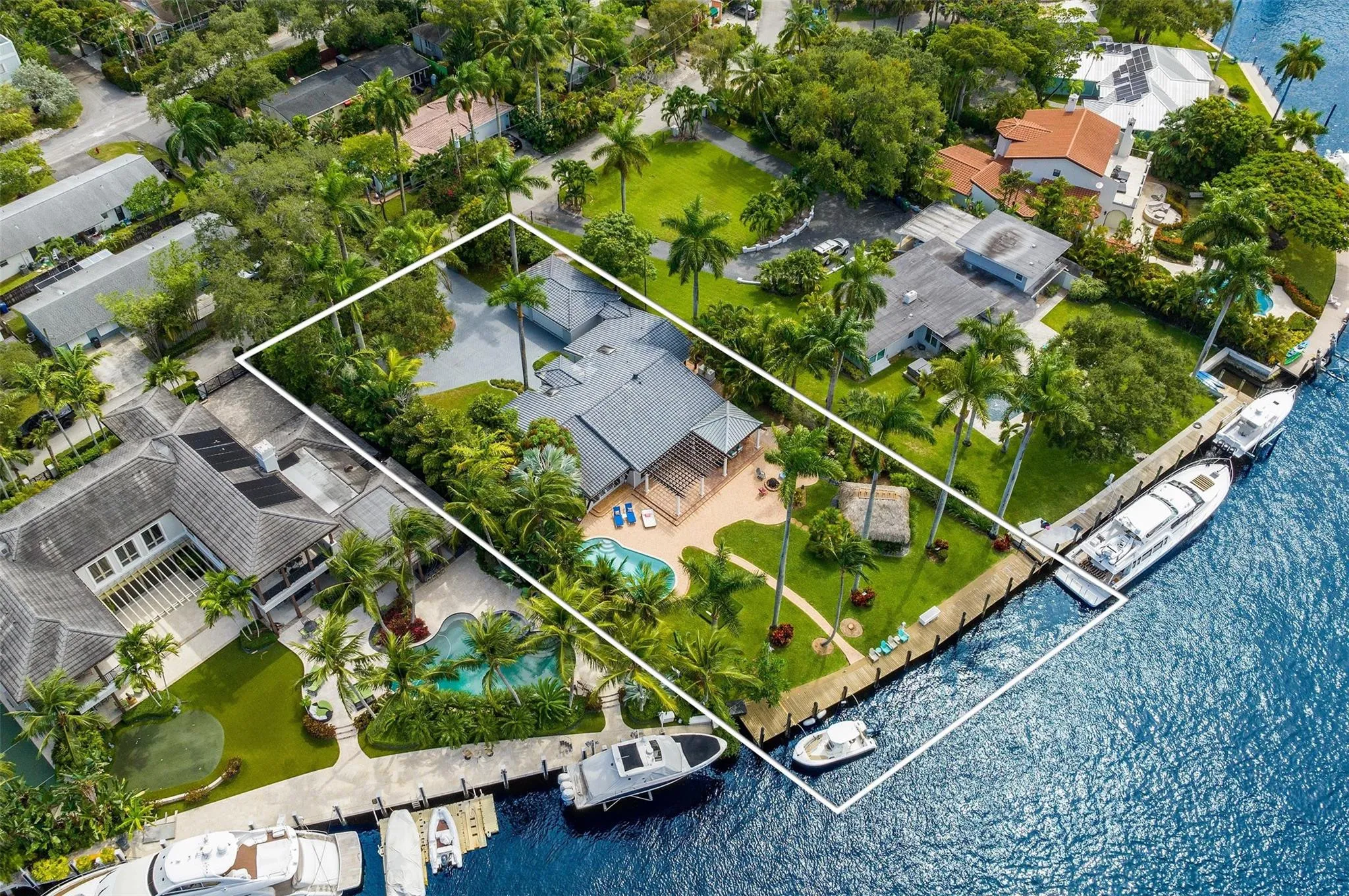 Waterfront property featuring a private dock, expansive green lawn, mature palm trees, and a swimming pool with integrated spa