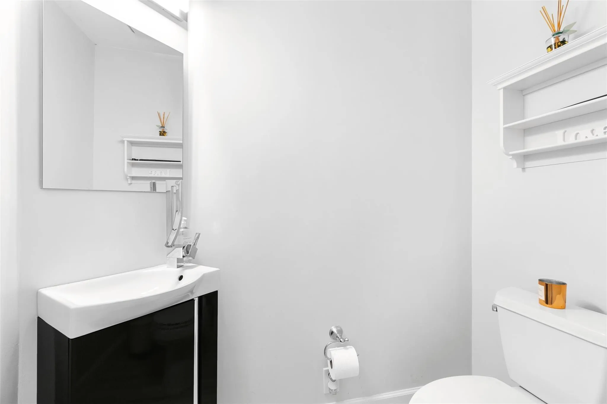 Compact bathroom featuring a modern wall-mounted sink with a black vanity cabinet, a rectangular mirror, a white toilet, and white wall shelving