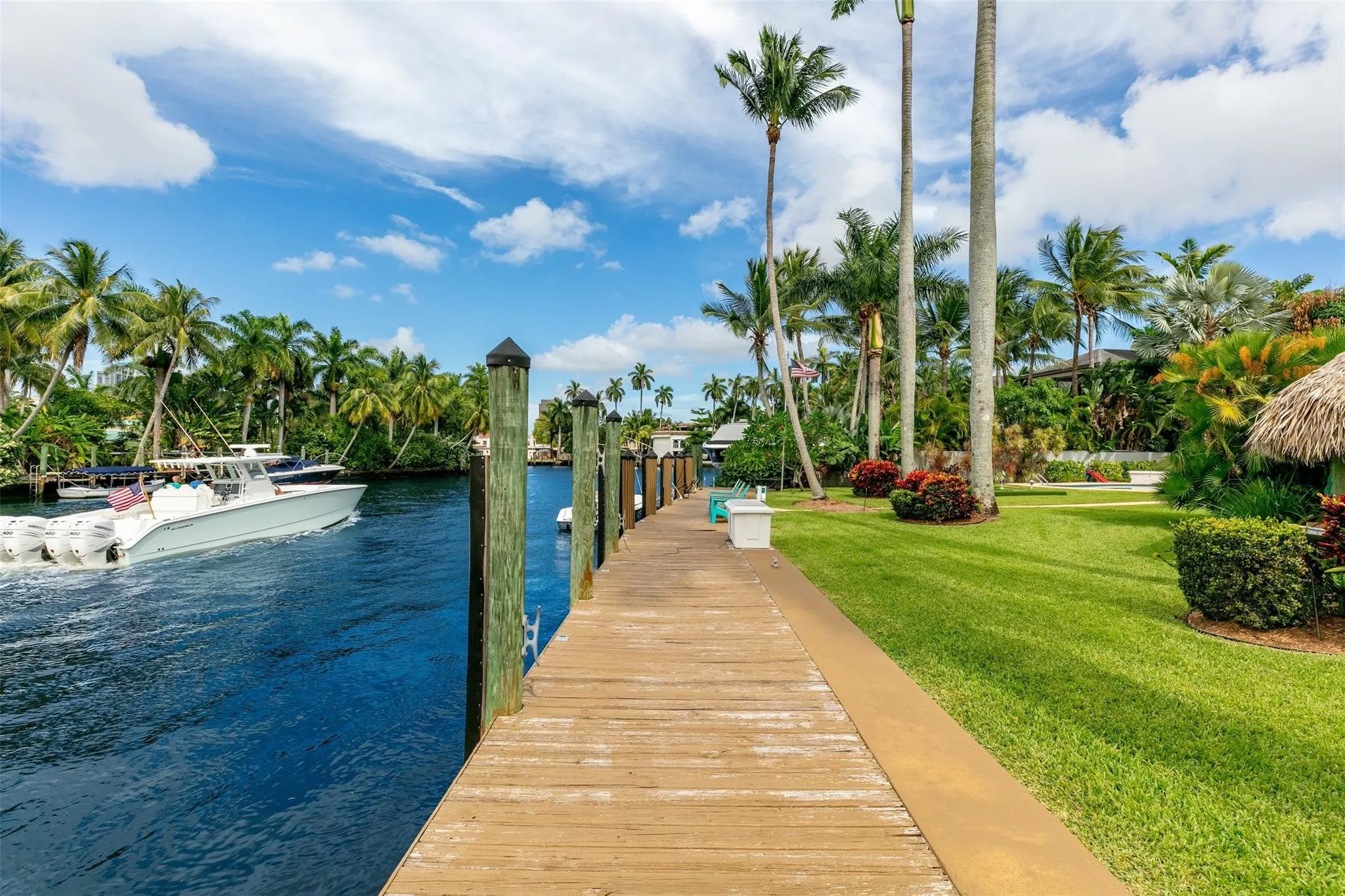 Private dock featuring multiple pilings, direct water access, and a manicured lawn with mature palm trees