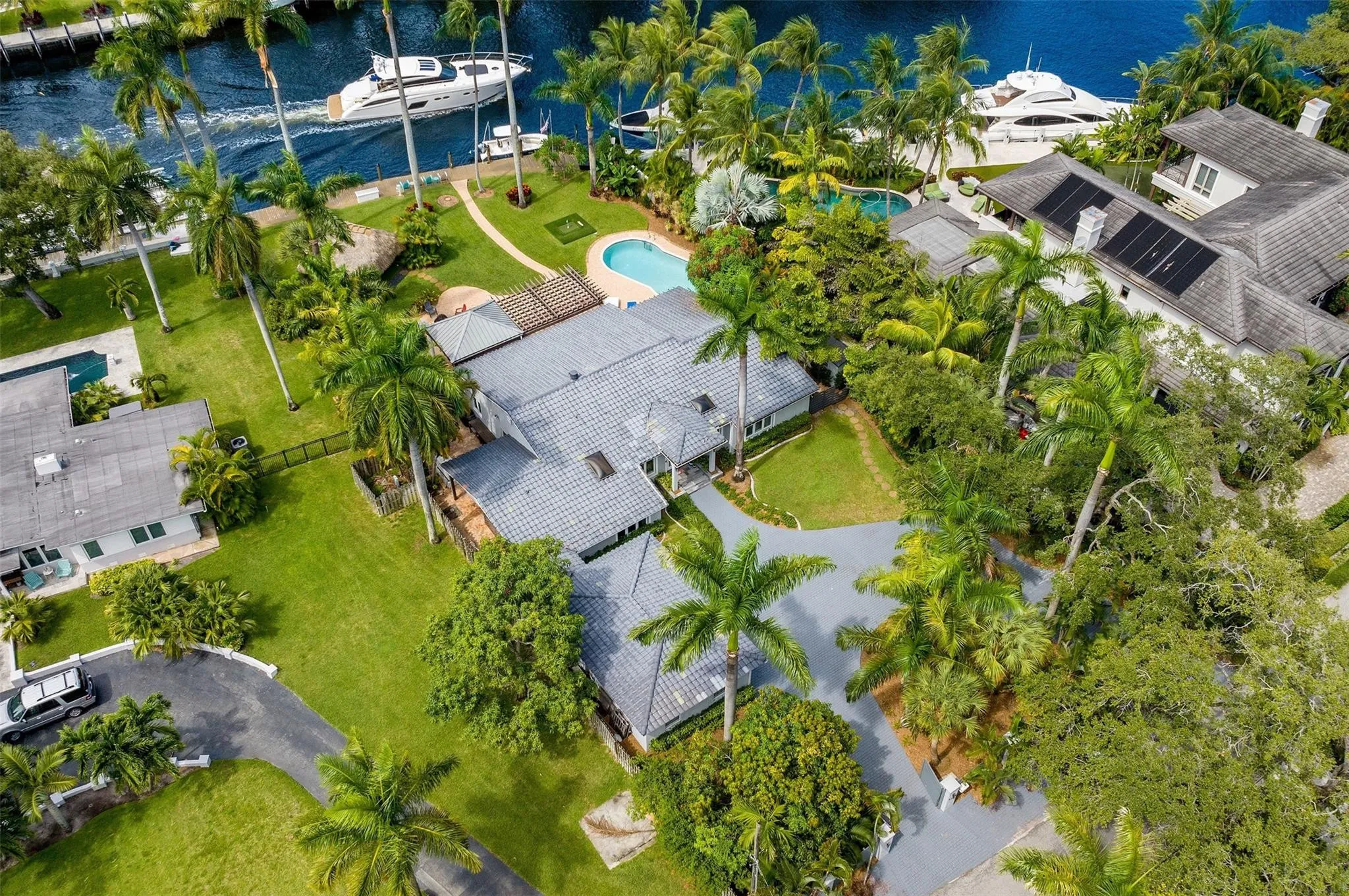 Expansive waterfront property featuring a private dock, swimming pool, mature palm trees, and lush landscaping