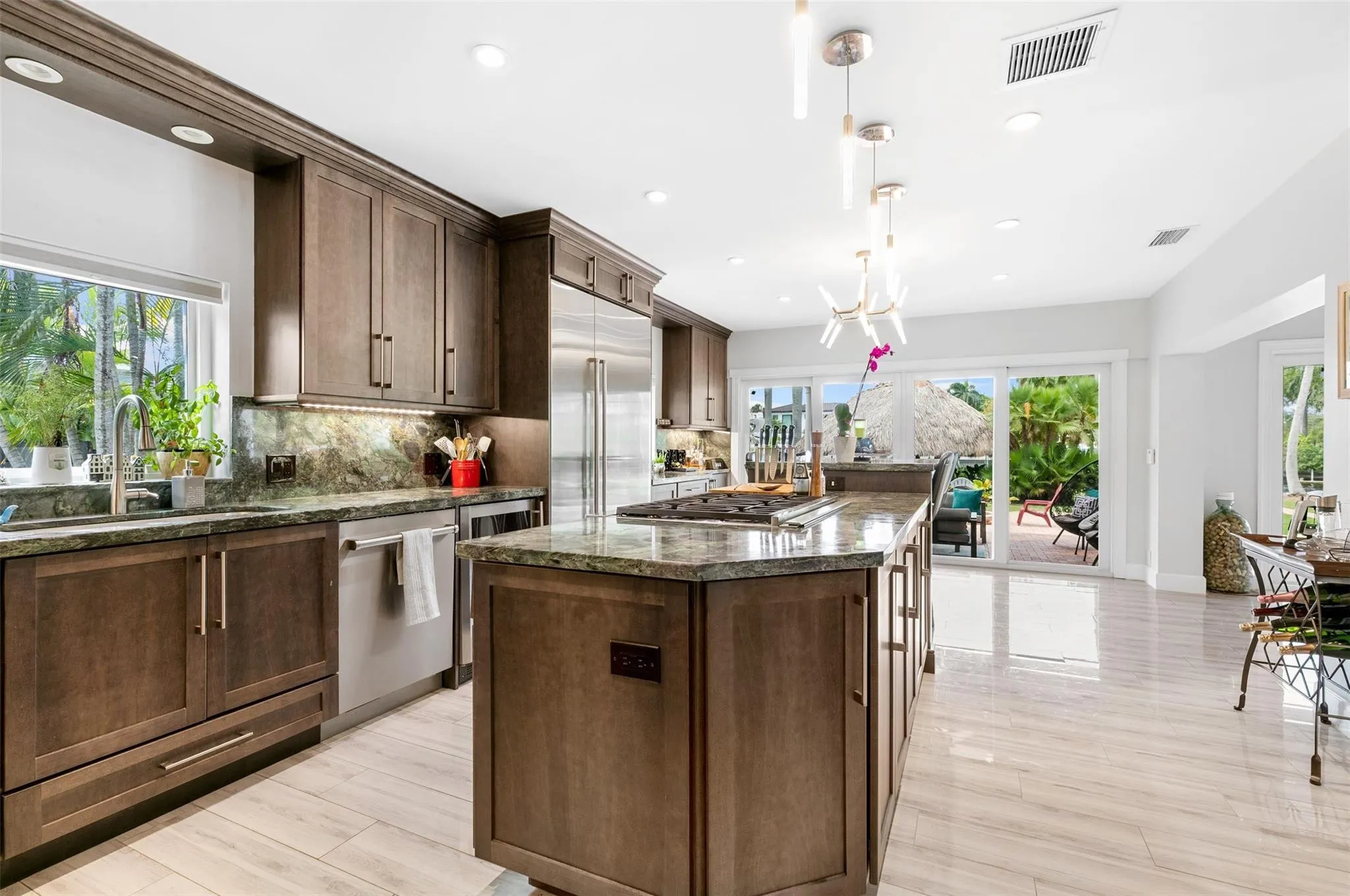 Spacious kitchen featuring dark wood cabinetry, stainless steel appliances, a large center island with cooktop, and light-toned tile flooring