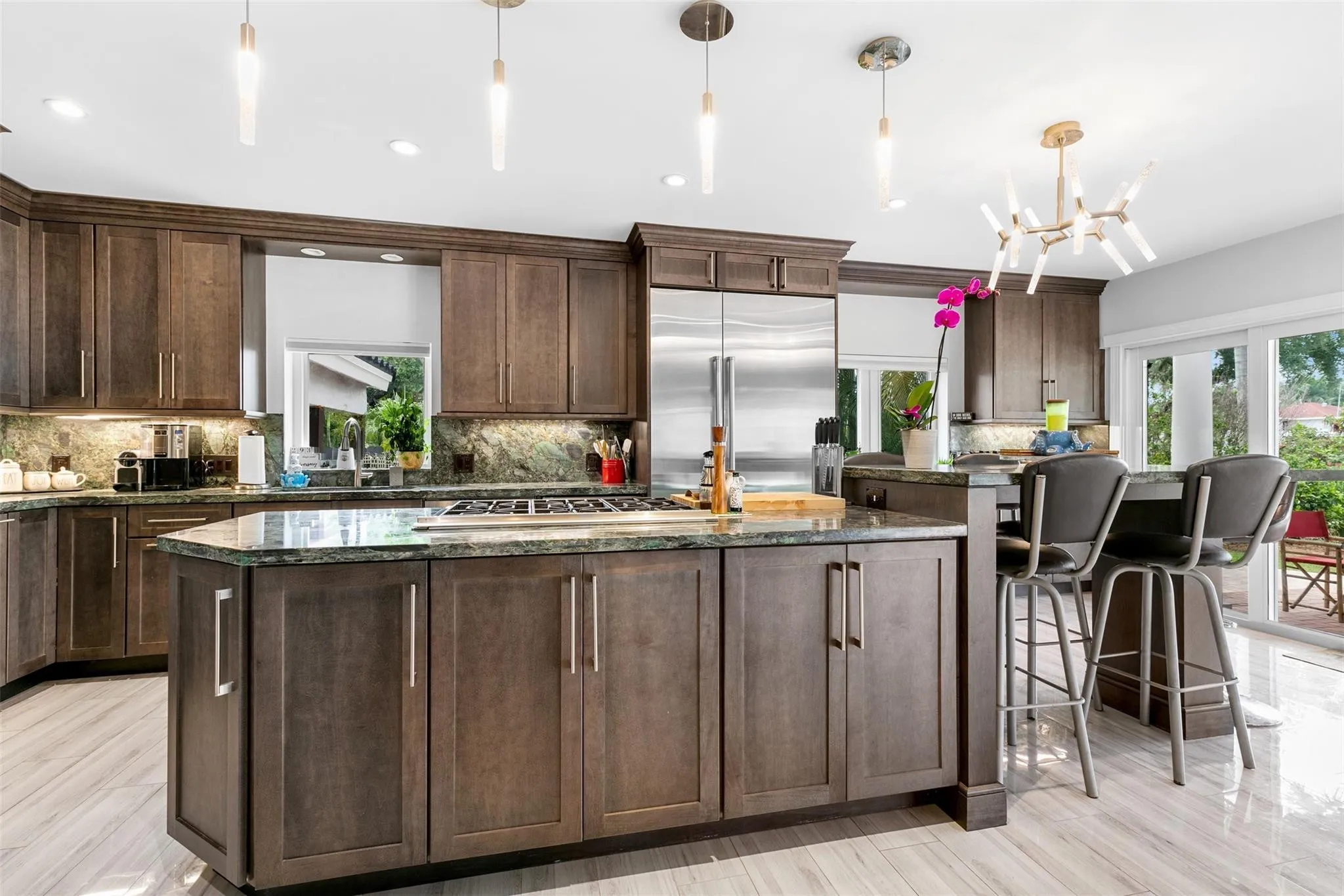 Open-concept kitchen featuring an oversized island with cooktop, stainless steel appliances, dark wood-finish cabinetry, and light wood-finish flooring