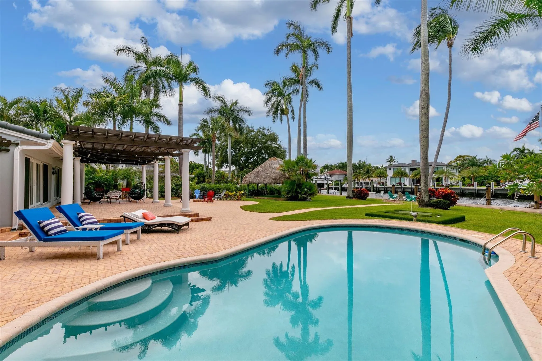 Outdoor oasis featuring a curved swimming pool with integrated steps, surrounded by brick-patterned hardscaping