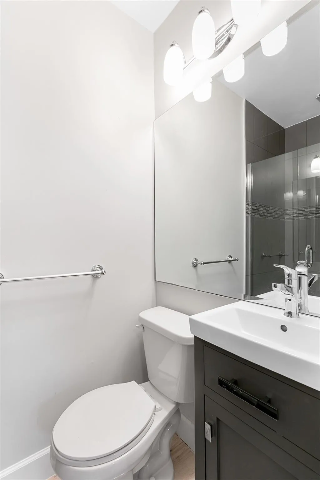 Bathroom featuring a white toilet, chrome towel bar, and a vanity with a white rectangular sink and dark cabinetry
