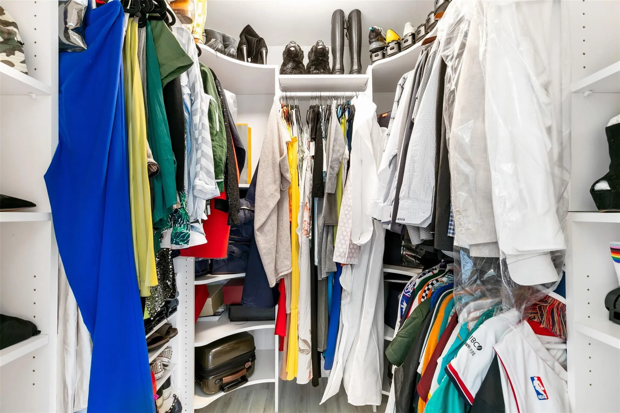 Walk-in closet with built-in shelving, multiple hanging rods, corner shelving, and light wood-finish flooring