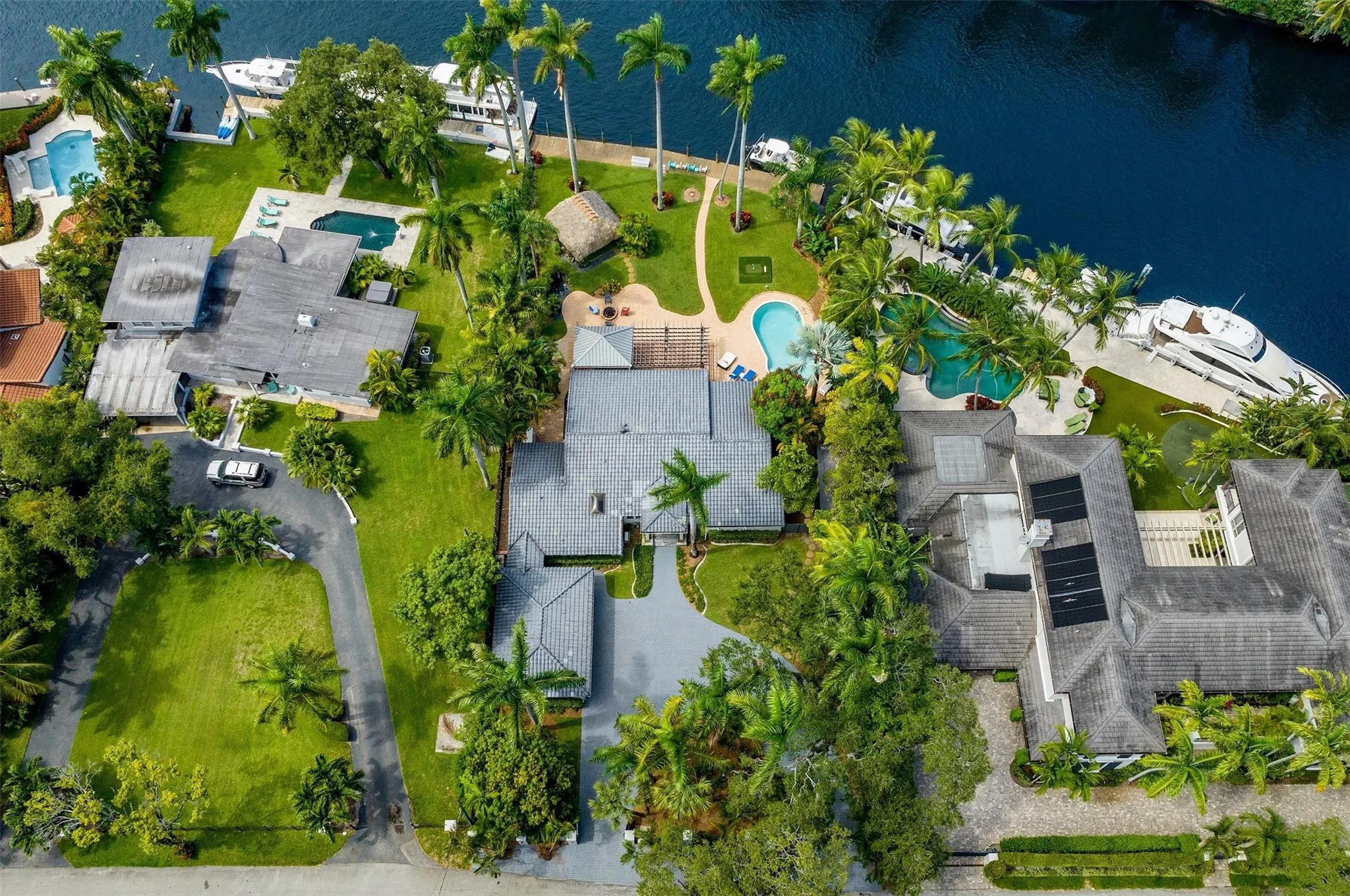 Waterfront property featuring a private dock, expansive green space, mature palm trees, and an irregularly shaped swimming pool
