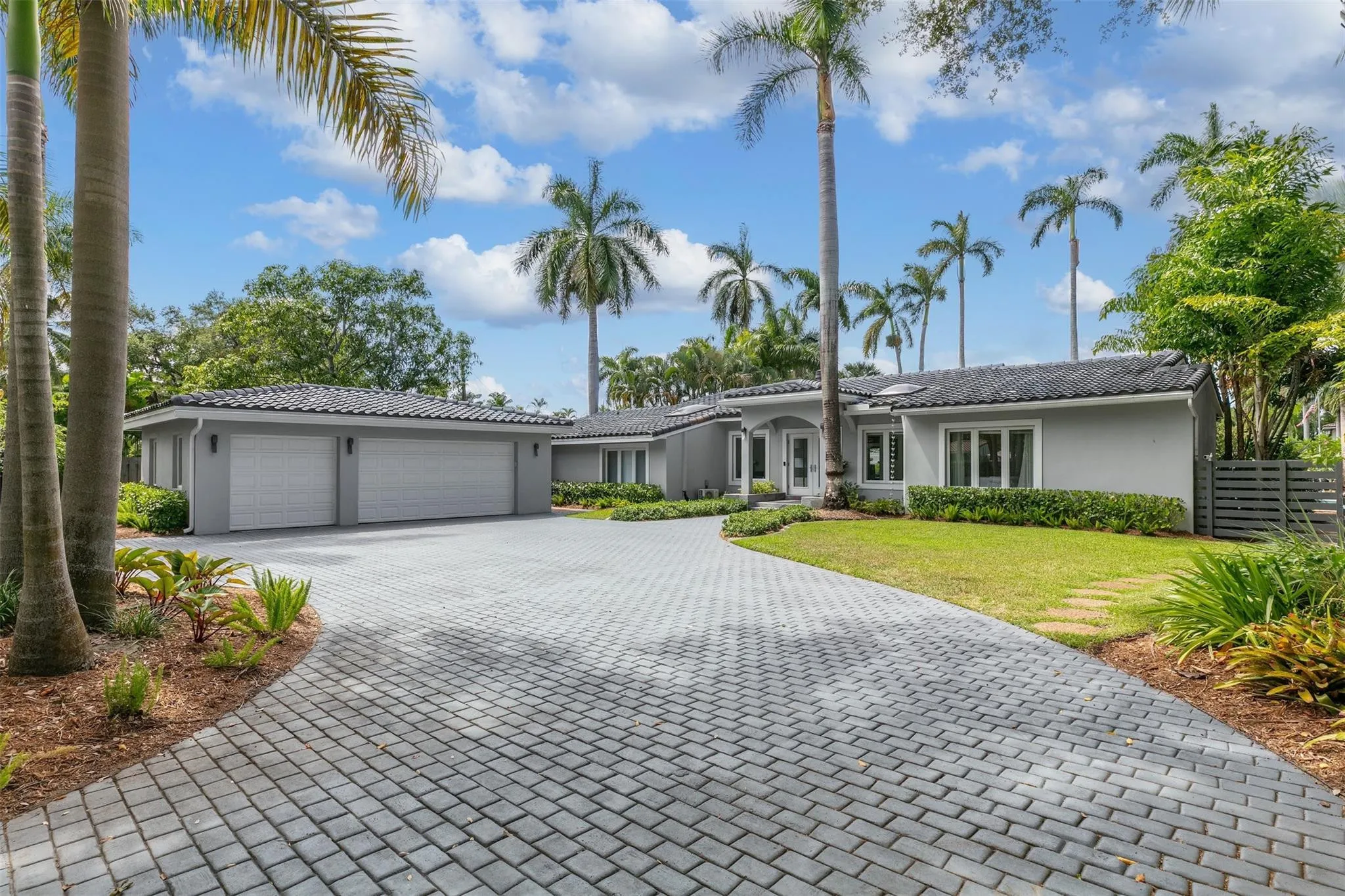 Paver driveway leading to a residence with a light gray facade, dark tile roof, and a two-car garage