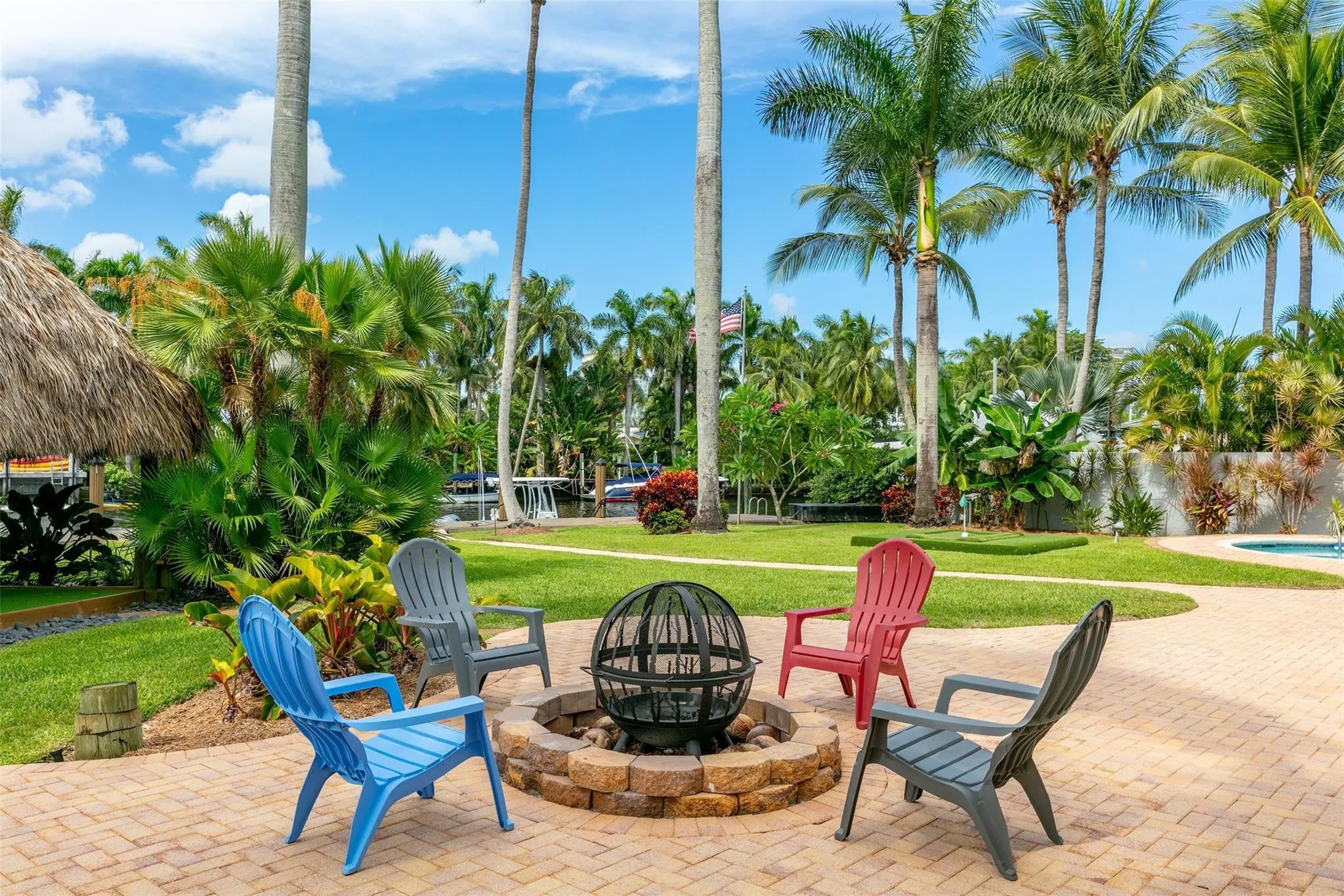 Brick paver patio with a built-in stone fire pit, surrounded by lush tropical landscaping and towering palm trees