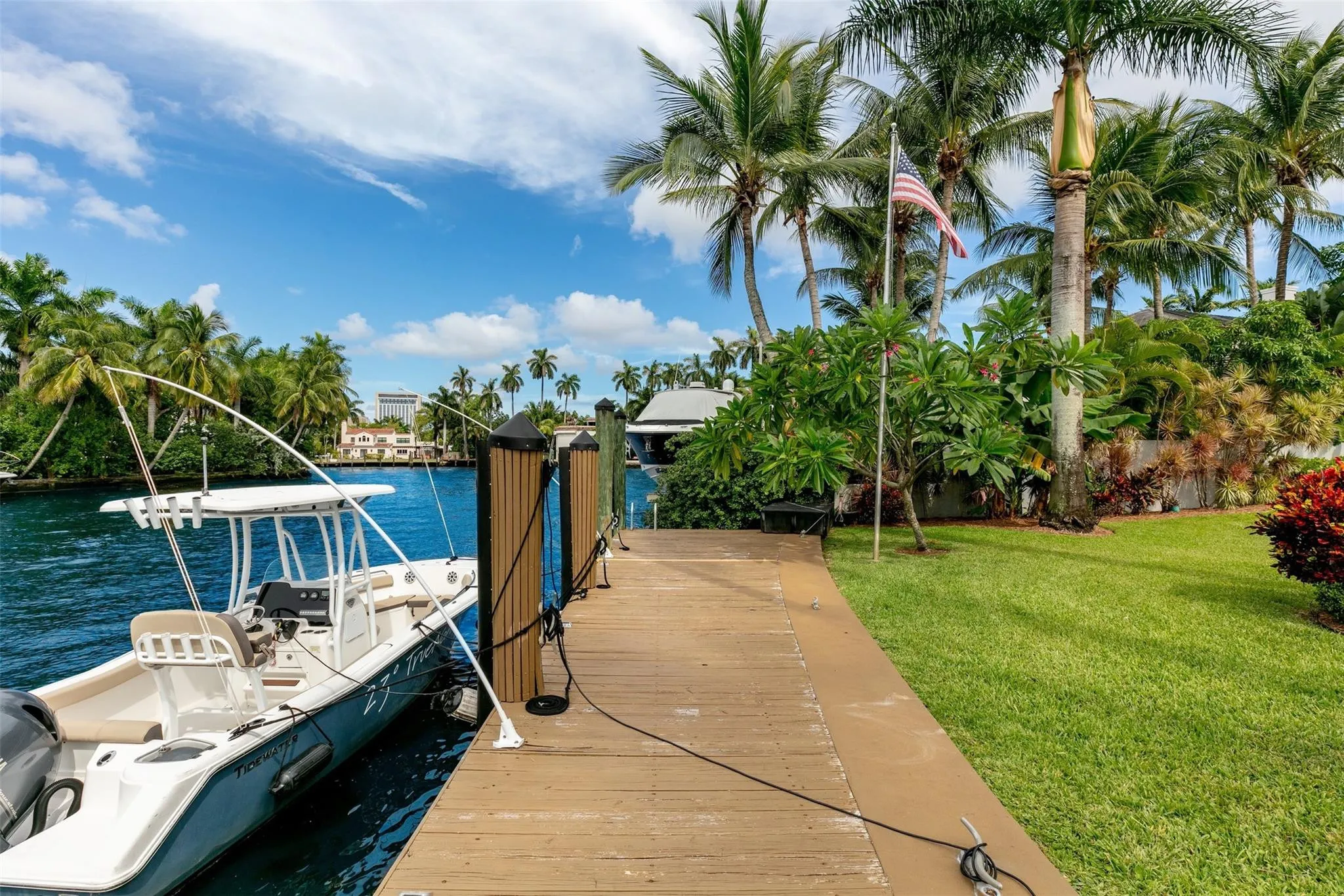 Waterfront property featuring a private wooden dock, lush tropical landscaping, mature palm trees, and a manicured lawn
