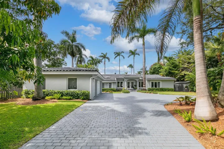 Contemporary residence featuring a paver driveway, lush tropical landscaping, mature palm trees, and a tiled roof