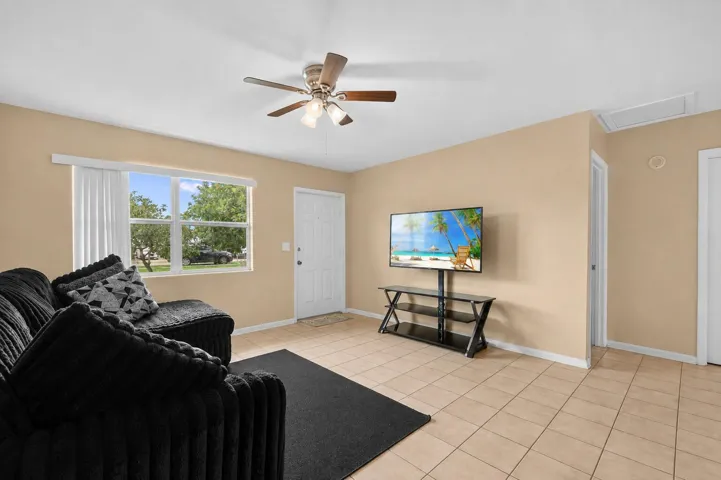 Living area featuring neutral-toned walls, tile flooring, a window offering exterior views, and a ceiling fan with integrated lighting