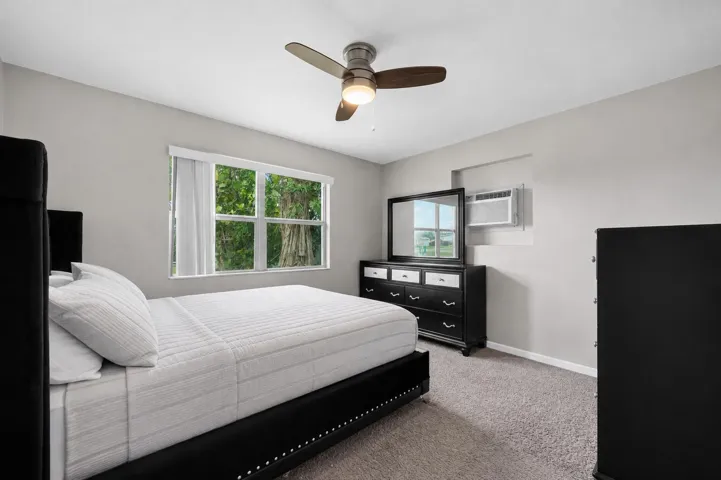 Broadloom carpeted room featuring a window with exterior tree views, a ceiling fan with integrated lighting, and a wall-mounted air conditioning unit