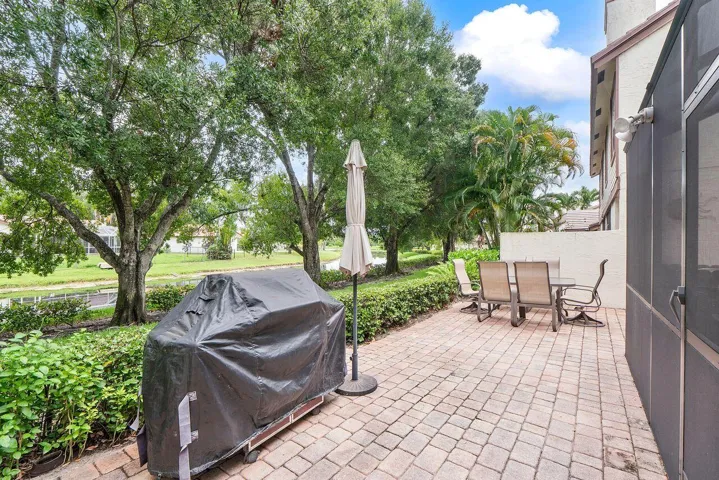 Expansive paved patio with a perimeter hedge and mature trees