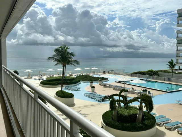 Expansive outdoor living area featuring a resort-style pool deck, multiple swimming pools, manicured landscaping with palm trees, and direct beach access