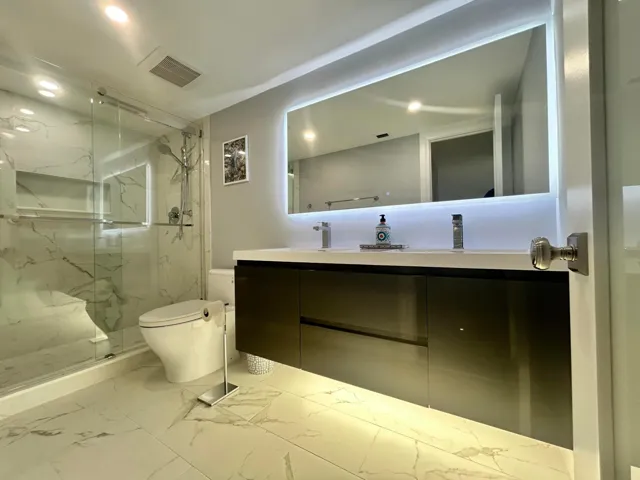 Spa-inspired primary bathroom featuring a floating vanity with dual vessel sinks, LED-backlit mirror, and polished stone-finish flooring
