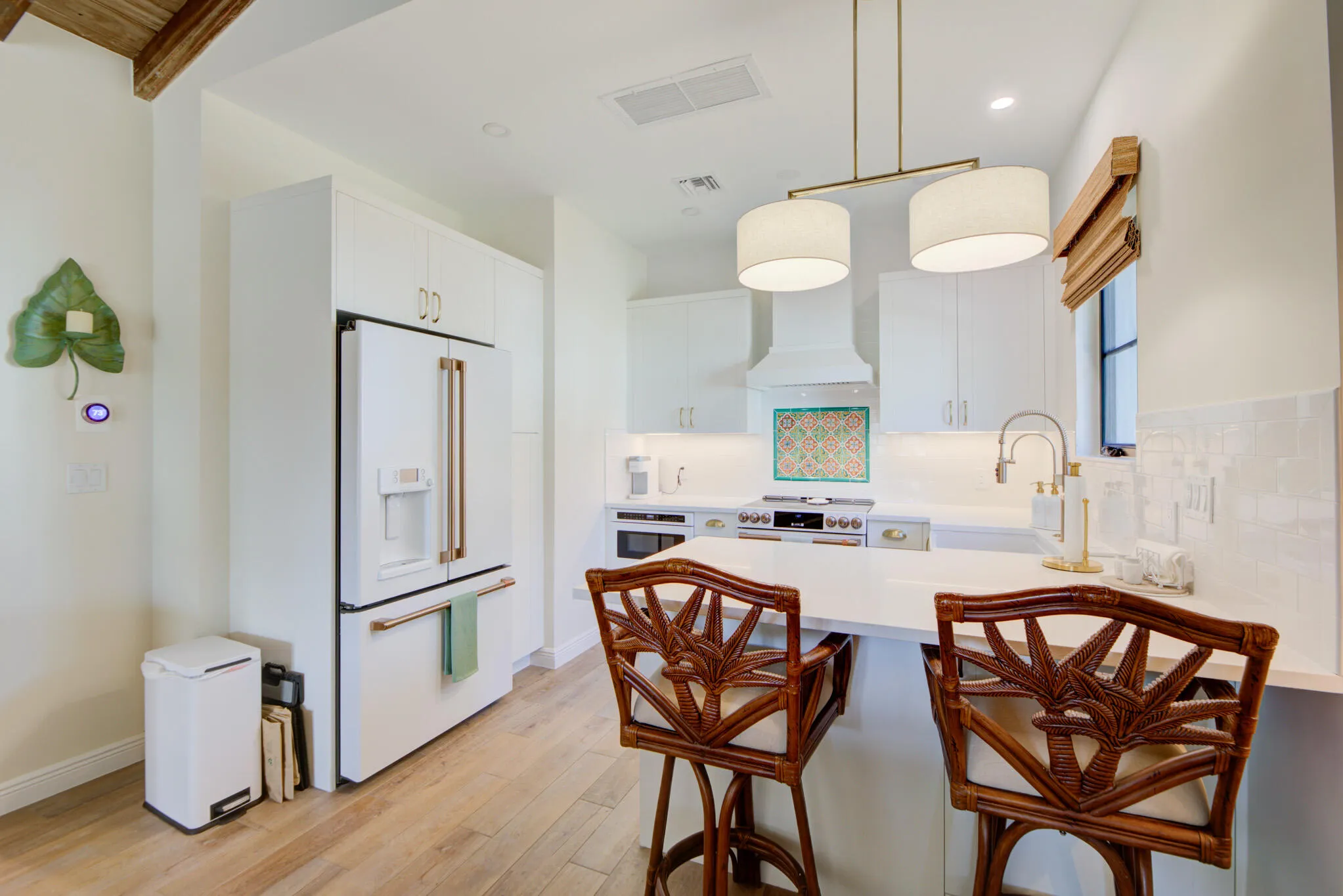 Modern kitchen featuring white cabinetry, a white GE Cafe refrigerator with brass-toned hardware, wood-finish flooring, and a stone countertop