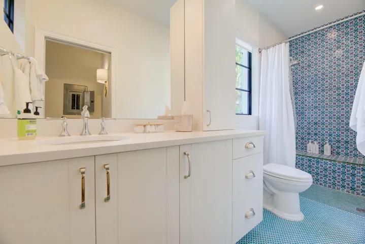 Bathroom featuring a patterned blue and white tile shower surround, matching floor tile, a built-in shower bench, and a window with dark framing