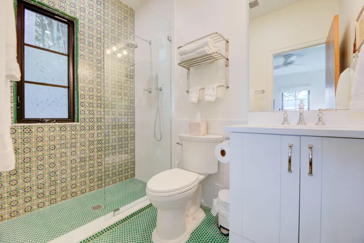 Bathroom featuring a walk-in shower with patterned tile surround and green mosaic floor