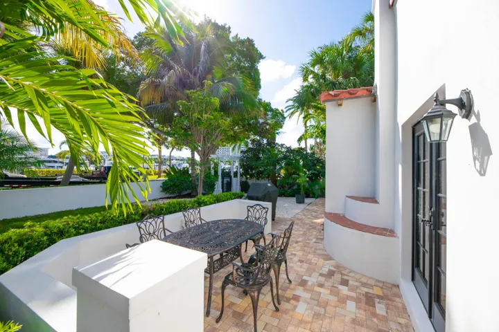 Outdoor patio featuring paver flooring, white stucco walls, and lush tropical landscaping