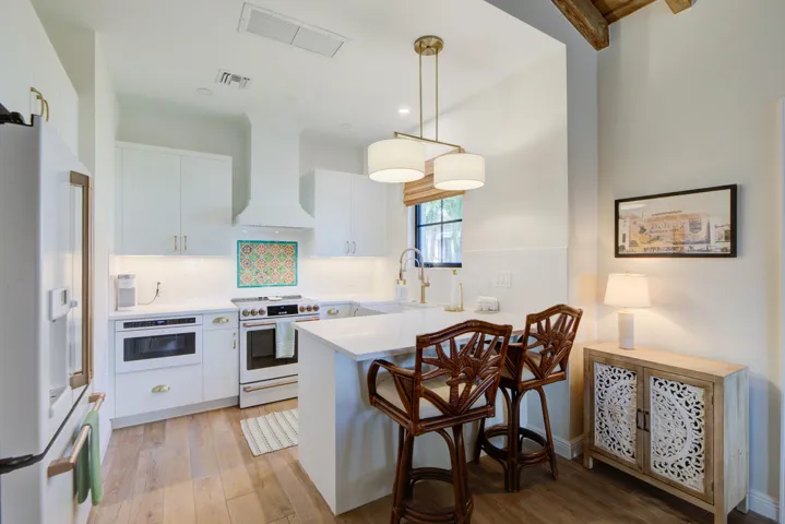 Bright kitchen featuring white cabinetry, a large center island with seating, pendant lighting, built-in drawer microwave, and wood-finish flooring