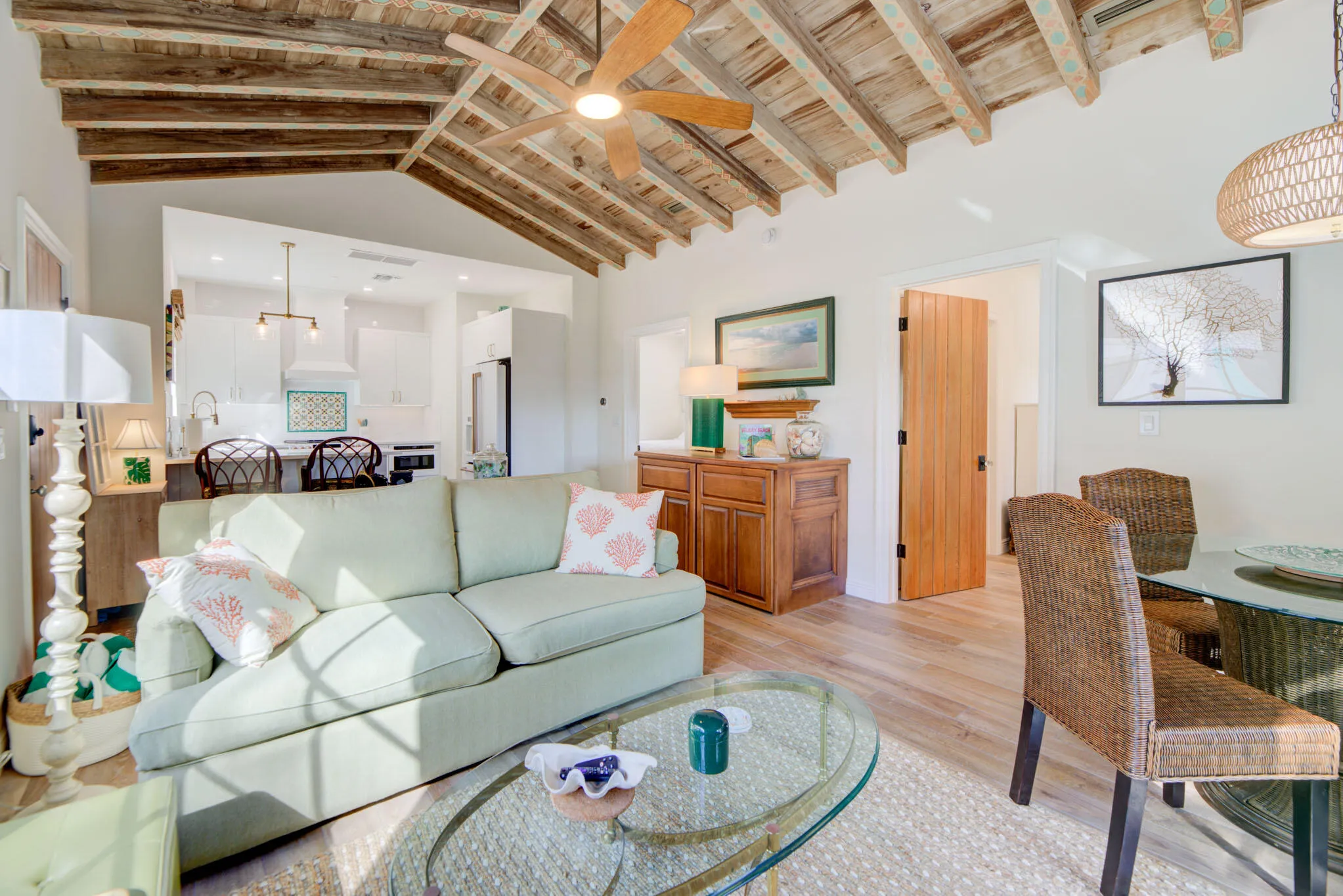 Vaulted wood-beam ceiling with natural finish, light wood-finish flooring, and a kitchen featuring white cabinetry, a built-in range hood, and a tiled backsplash