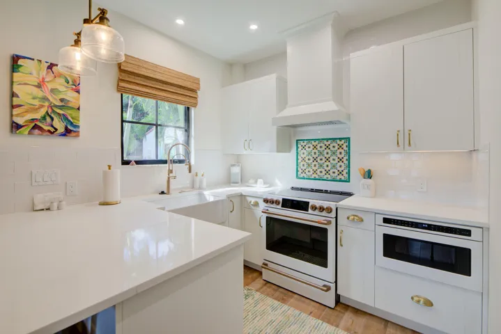Contemporary kitchen featuring white cabinetry, light-colored countertops, a built-in microwave, and a white range with a coordinating vent hood