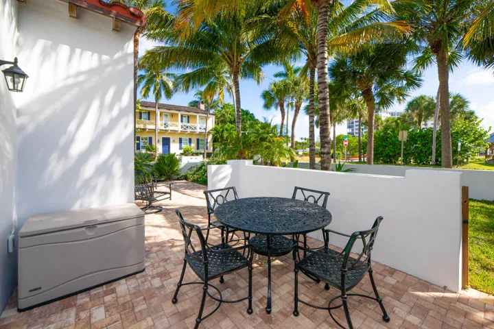 Paved patio area featuring white stucco walls, a wall-mounted light fixture, and mature palm trees