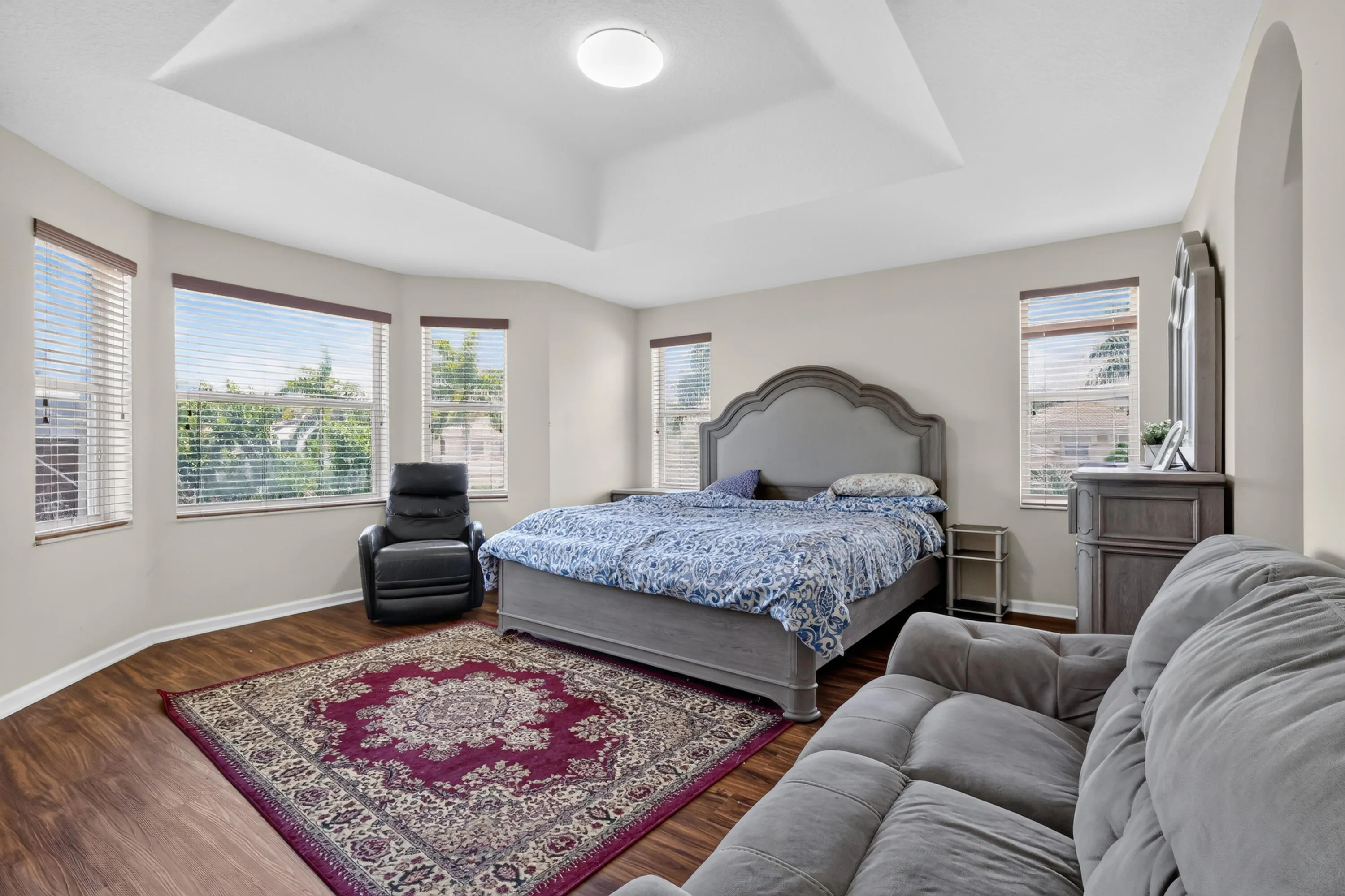 Spacious room featuring a tray ceiling, wood-finish flooring, and multiple windows with blinds