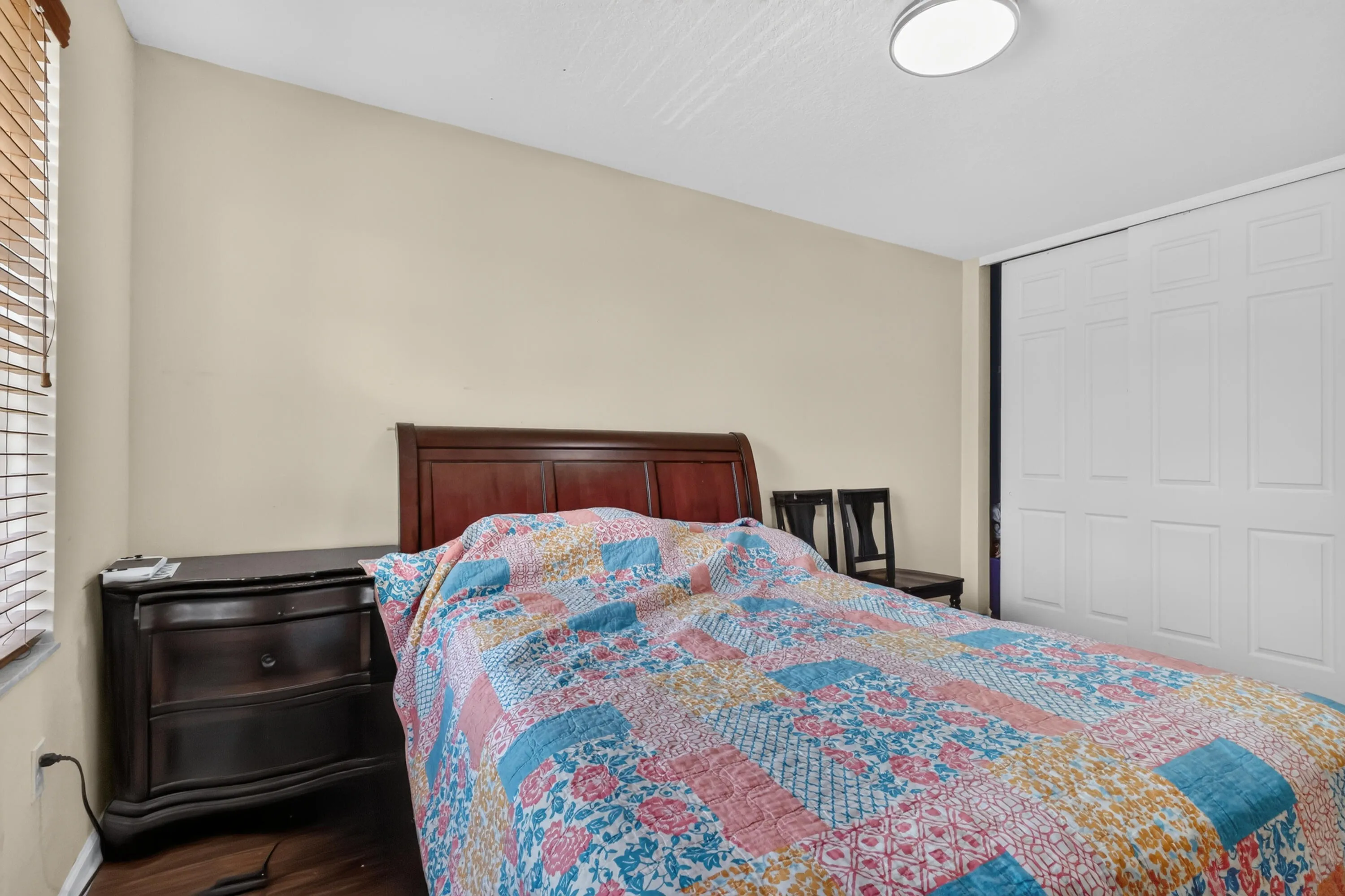 Spacious bedroom featuring wood-finish flooring, a contemporary flush-mount ceiling light, and white sliding closet doors