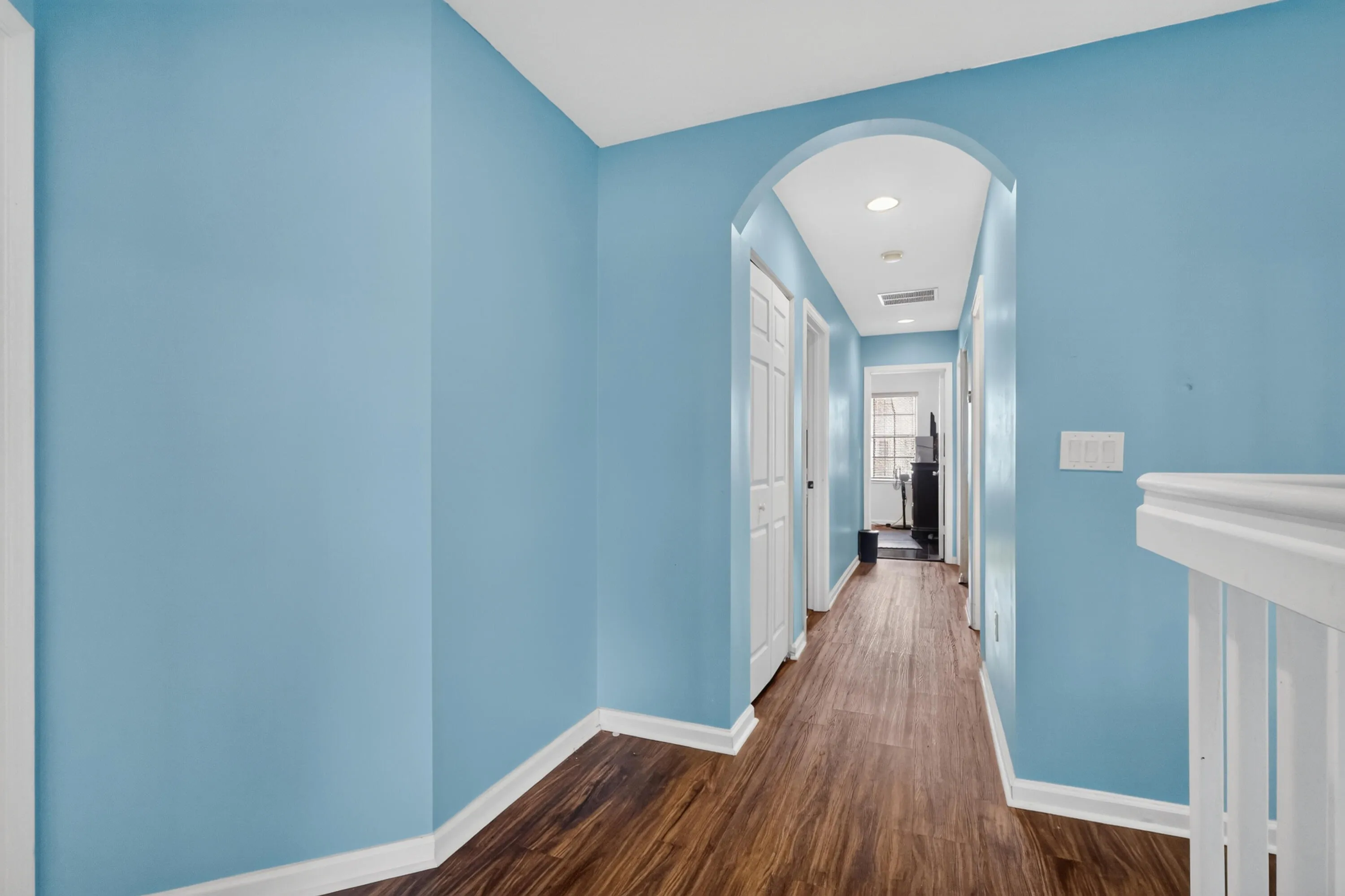 Hallway featuring soft blue walls, wood-finish flooring, and recessed ceiling lighting