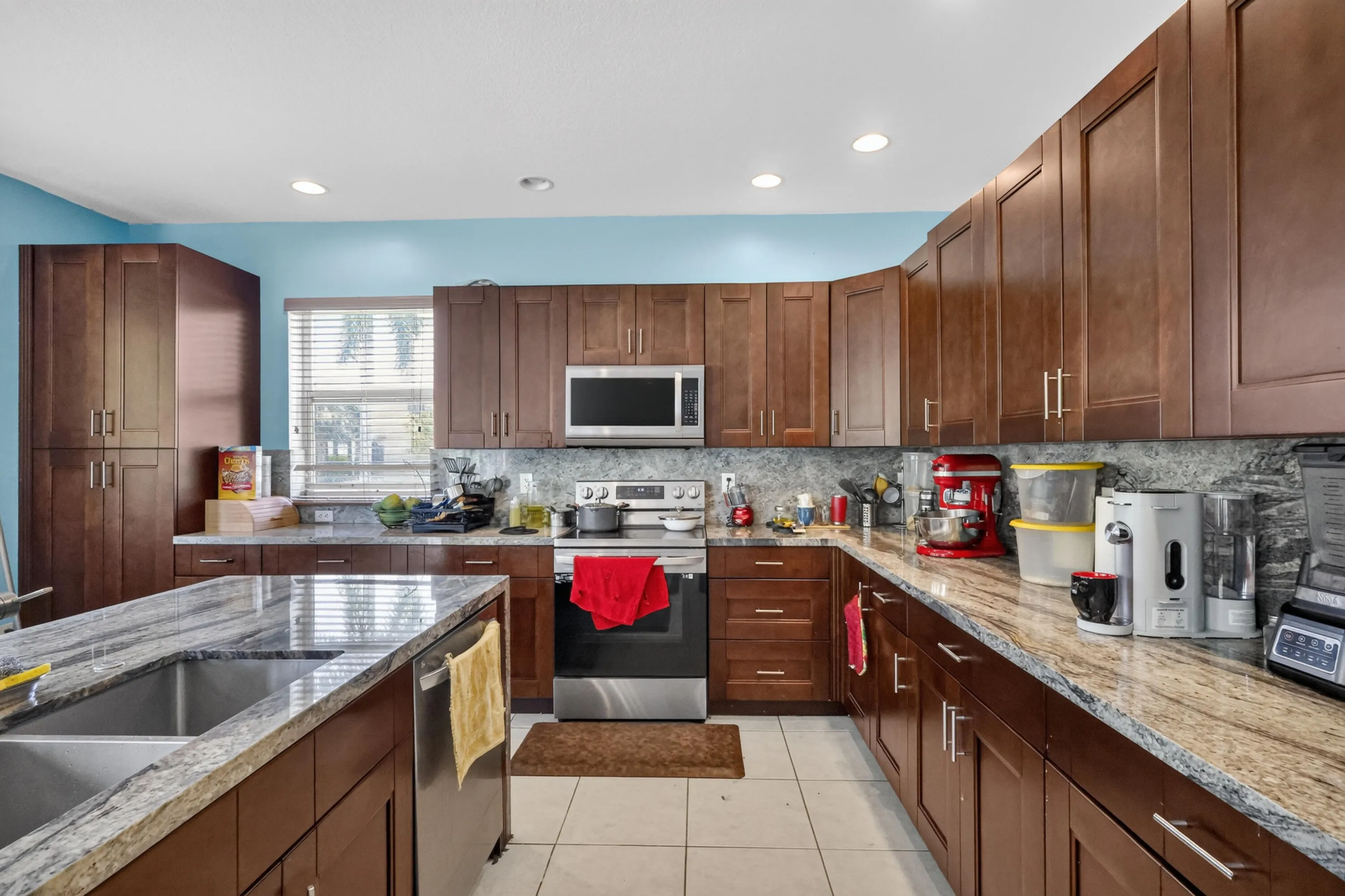 Kitchen featuring extensive wood-finish cabinetry, light-toned tile flooring, and integrated stainless steel appliances