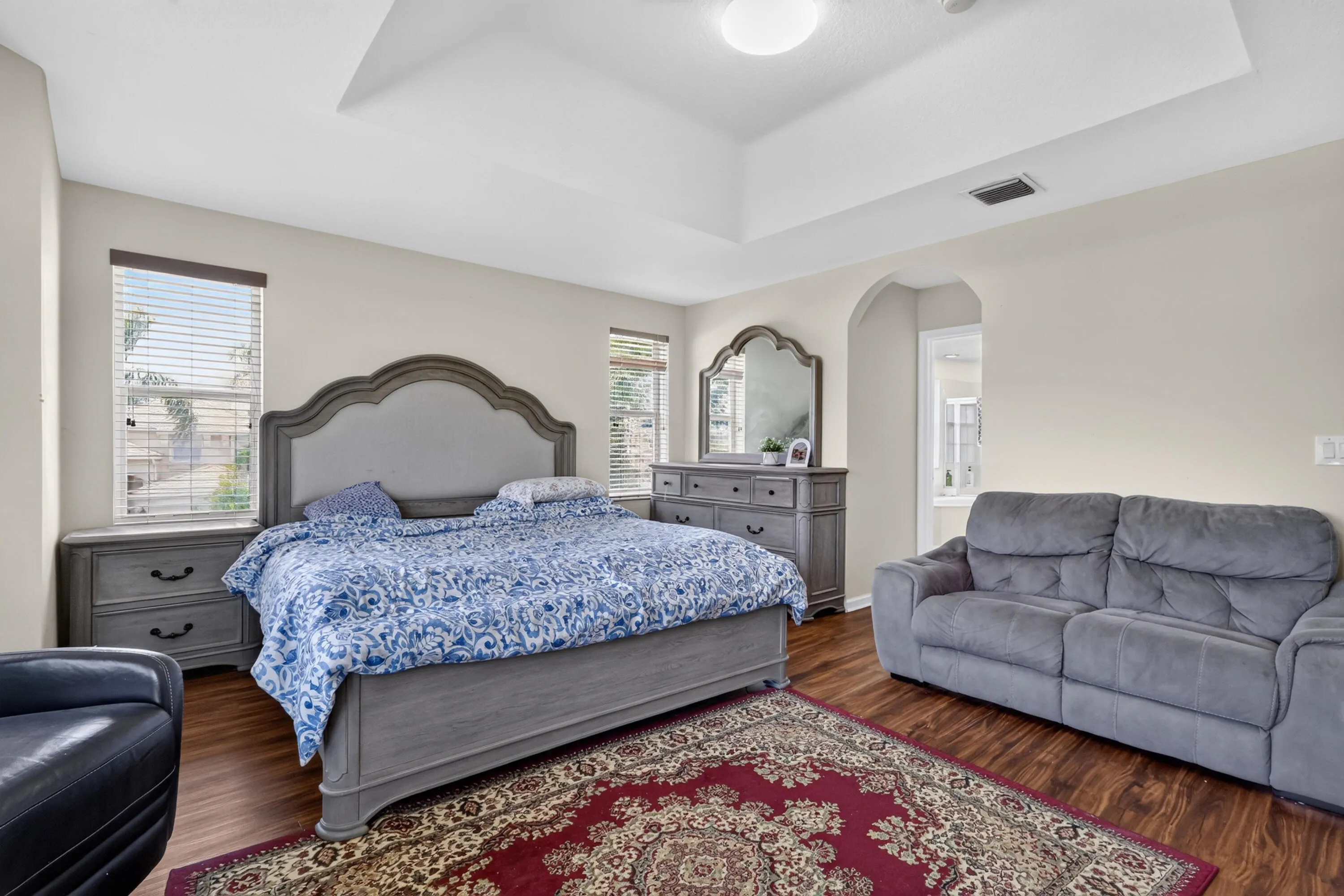 Spacious room featuring wood-finish flooring, a tray ceiling with recessed lighting, and multiple windows with blinds