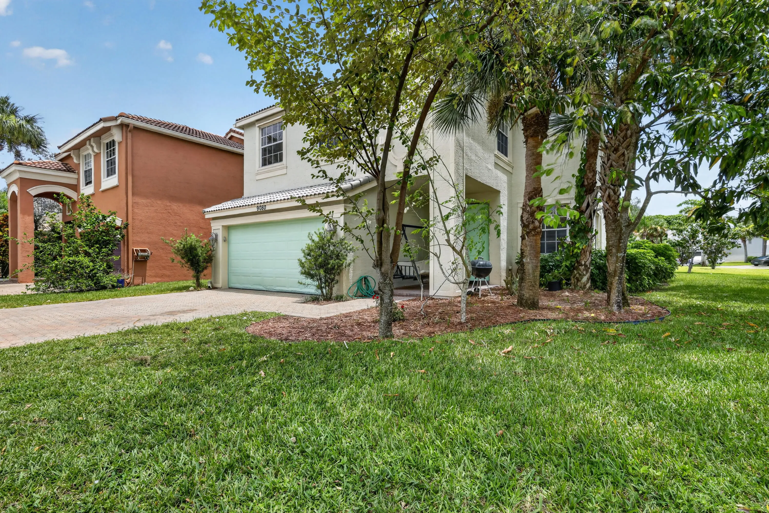 Exterior stucco residence featuring a light green garage door, a prominent front porch, and mature trees surrounding the property