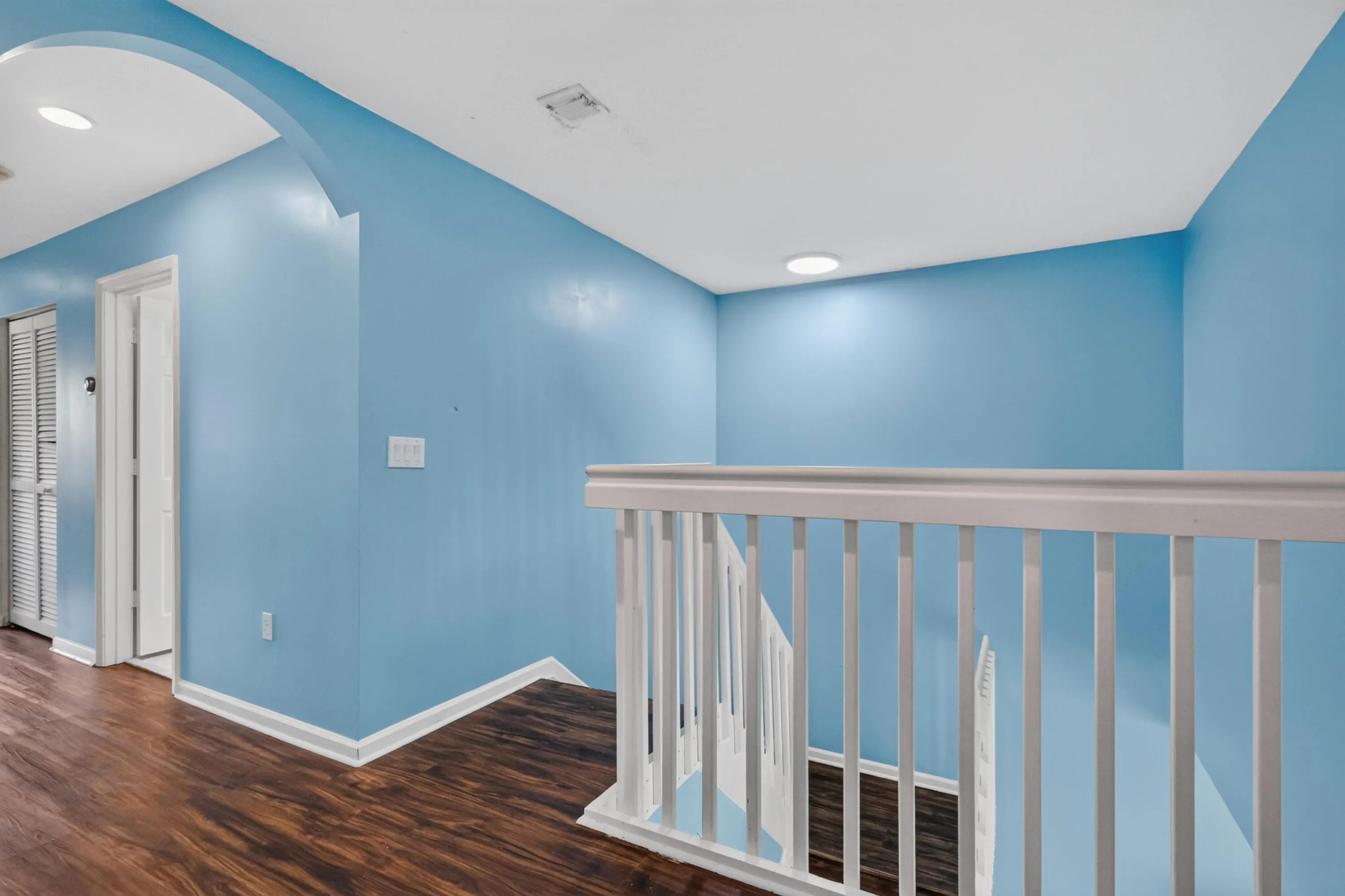 Upper-level hallway featuring wood-finish flooring, light blue walls, and a white balustrade