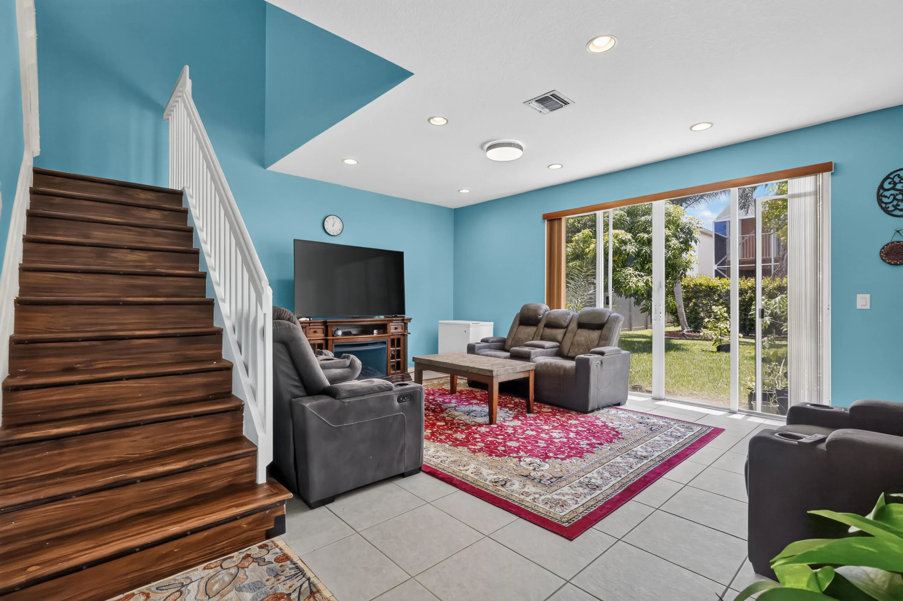 Hardwood staircase with white railing, tile flooring, recessed lighting, and sliding glass doors opening to a private backyard