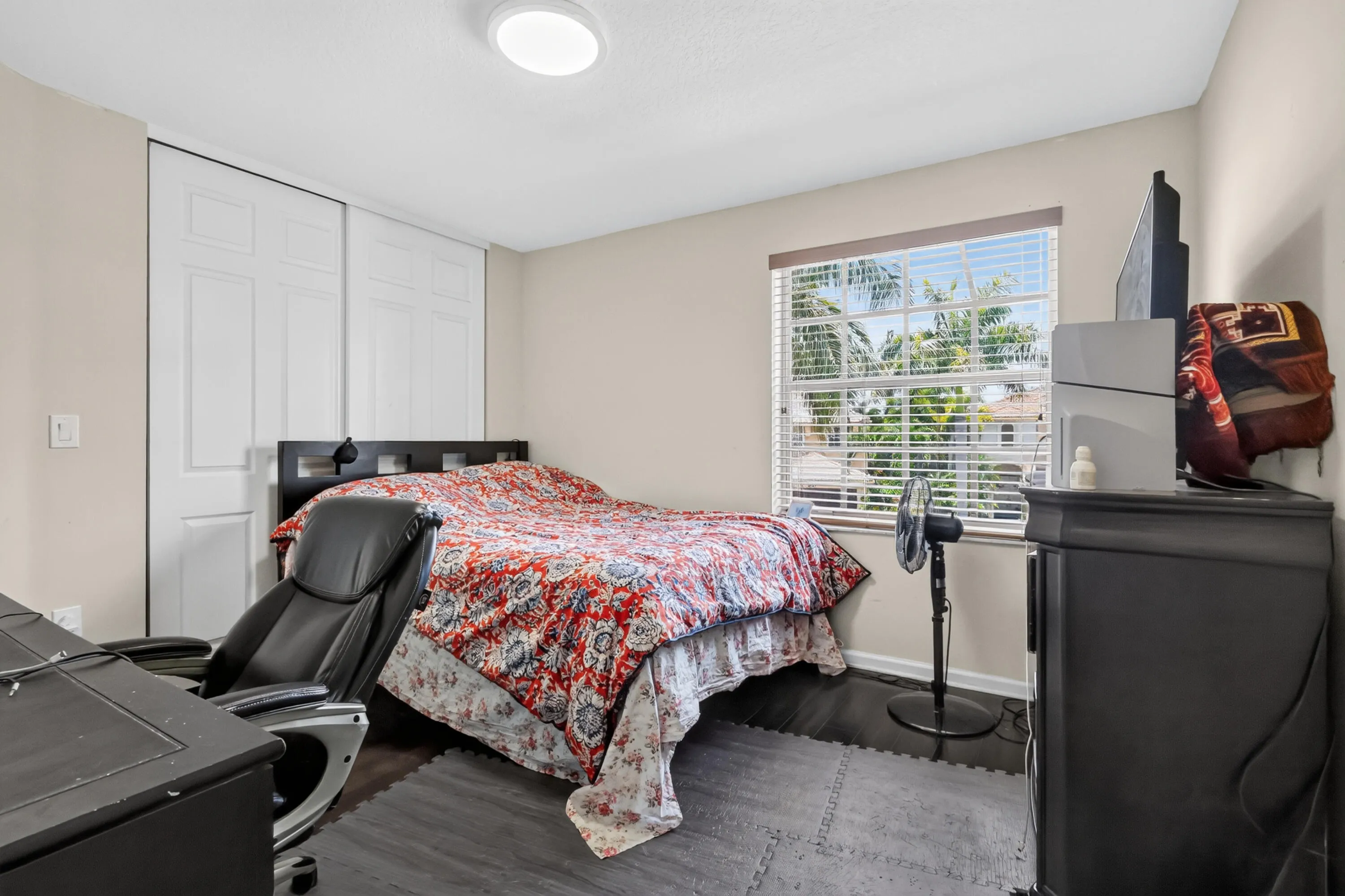 Bedroom featuring a window with blinds, dark wood-finish flooring, a built-in closet with bi-fold doors, and a ceiling-mounted light fixture