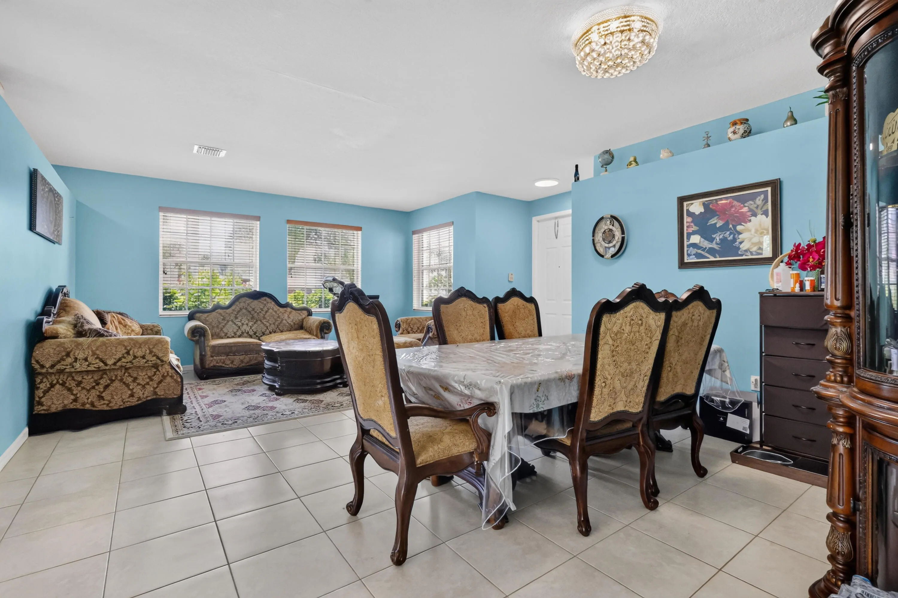 Open-concept living and dining area featuring tile flooring, multiple windows, a decorative ceiling light fixture, and a built-in wall niche