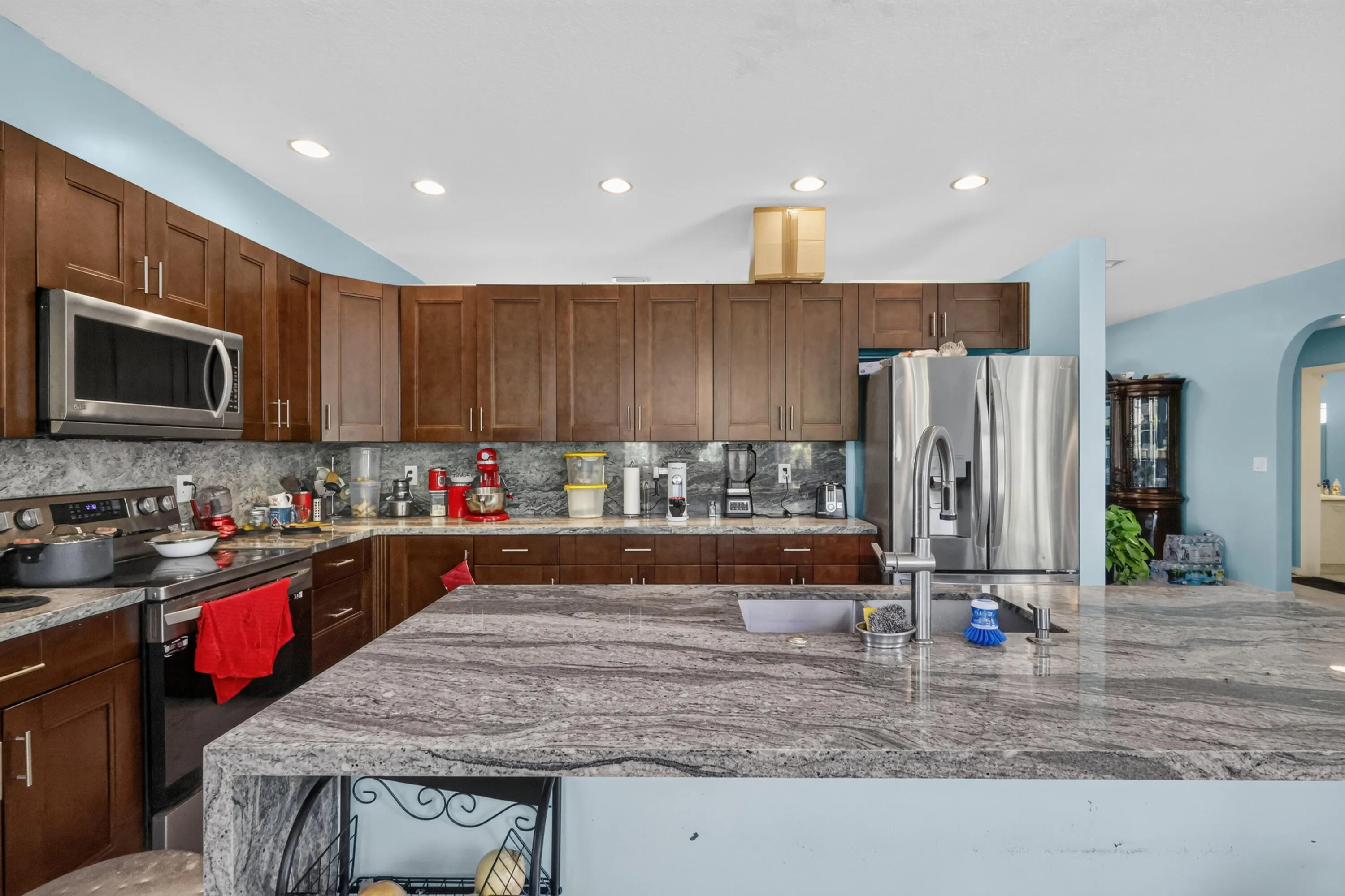 Kitchen featuring an expansive island with a stone countertop, dark wood-finish cabinetry, stainless steel appliances, and recessed lighting