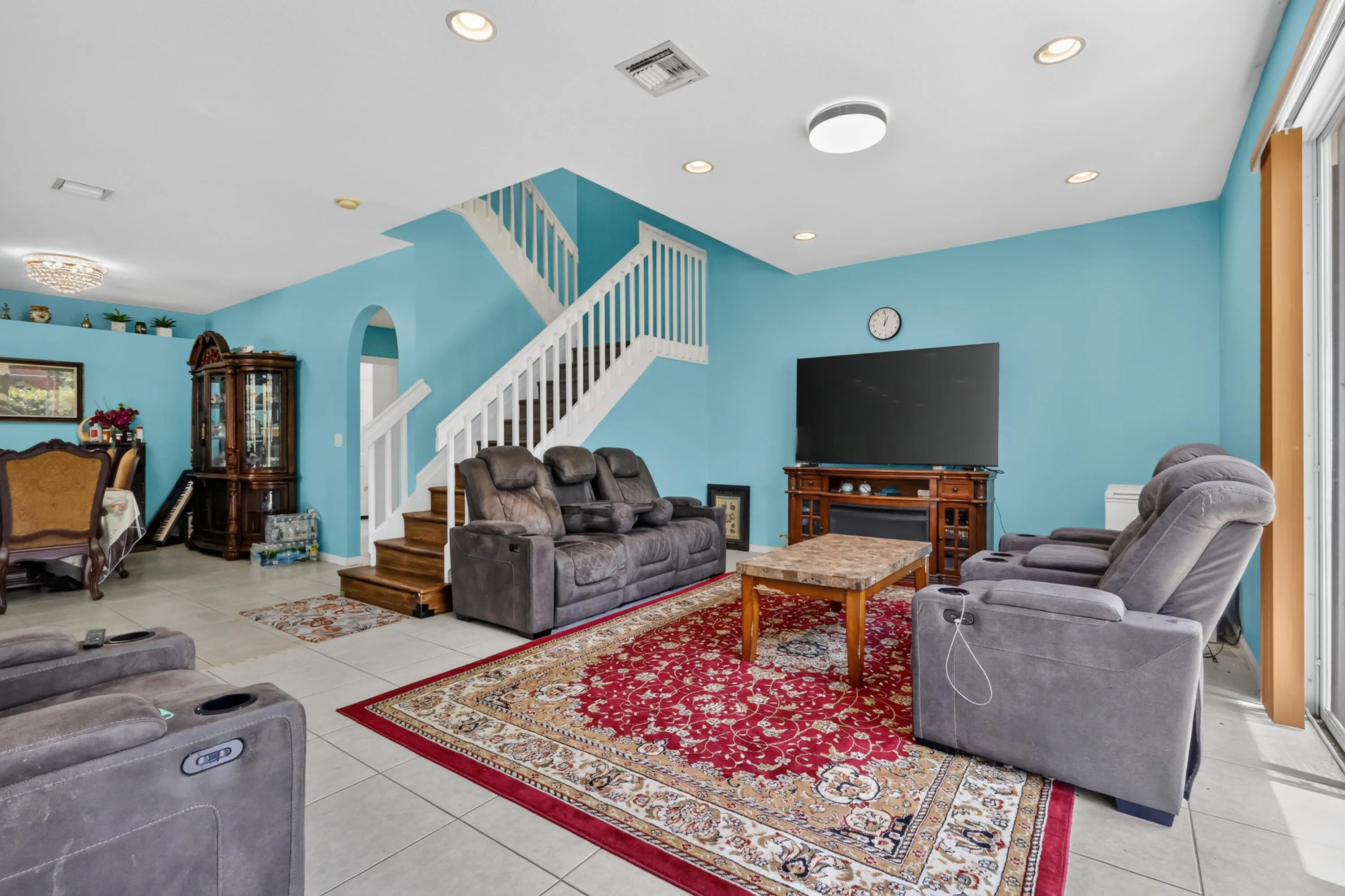 Open-concept living area featuring a prominent staircase with white railings, tile flooring, recessed lighting, and a built-in media console with an electric fireplace