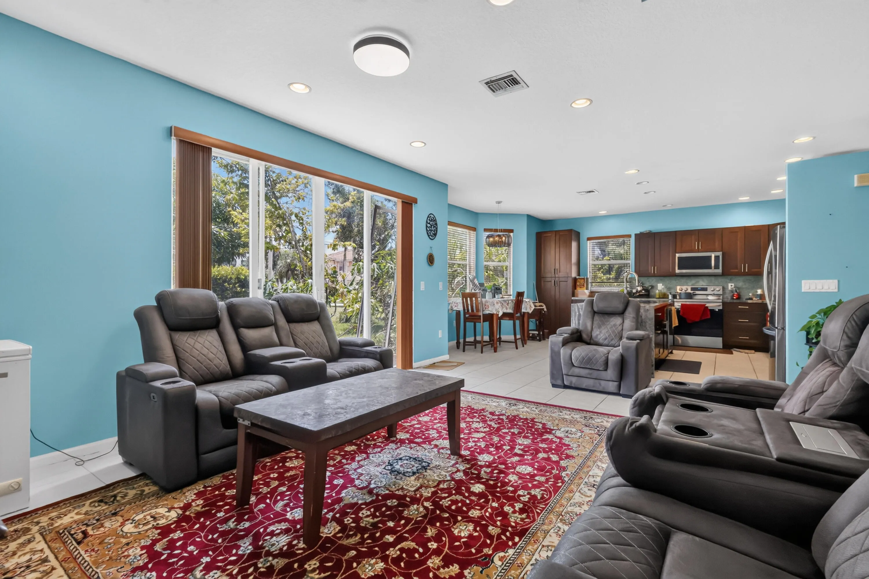 Open-concept living area with large glass sliding doors, recessed lighting, and a kitchen featuring wood cabinetry and stainless steel appliances