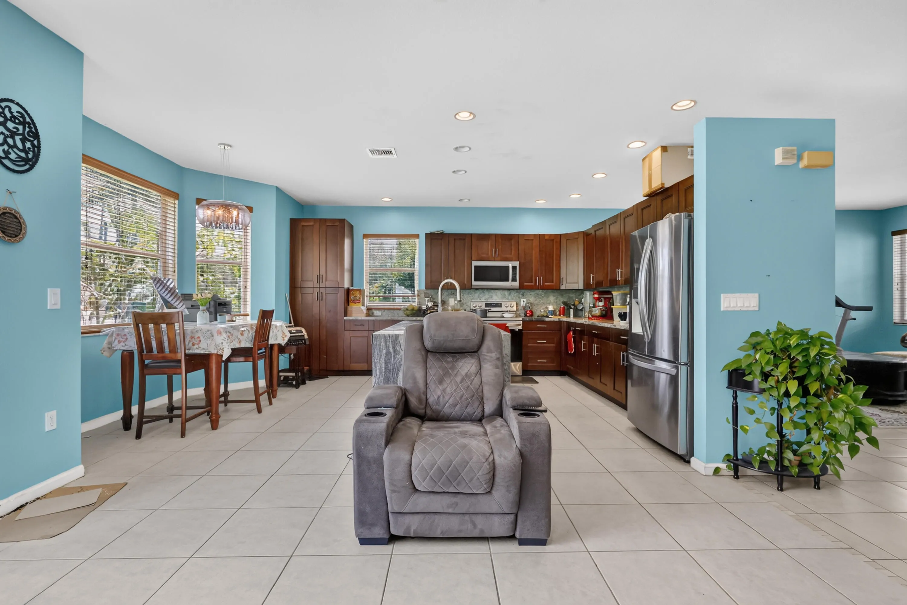 Open-concept kitchen and dining area featuring light-toned tile flooring, recessed lighting, wood cabinetry, and stainless steel appliances