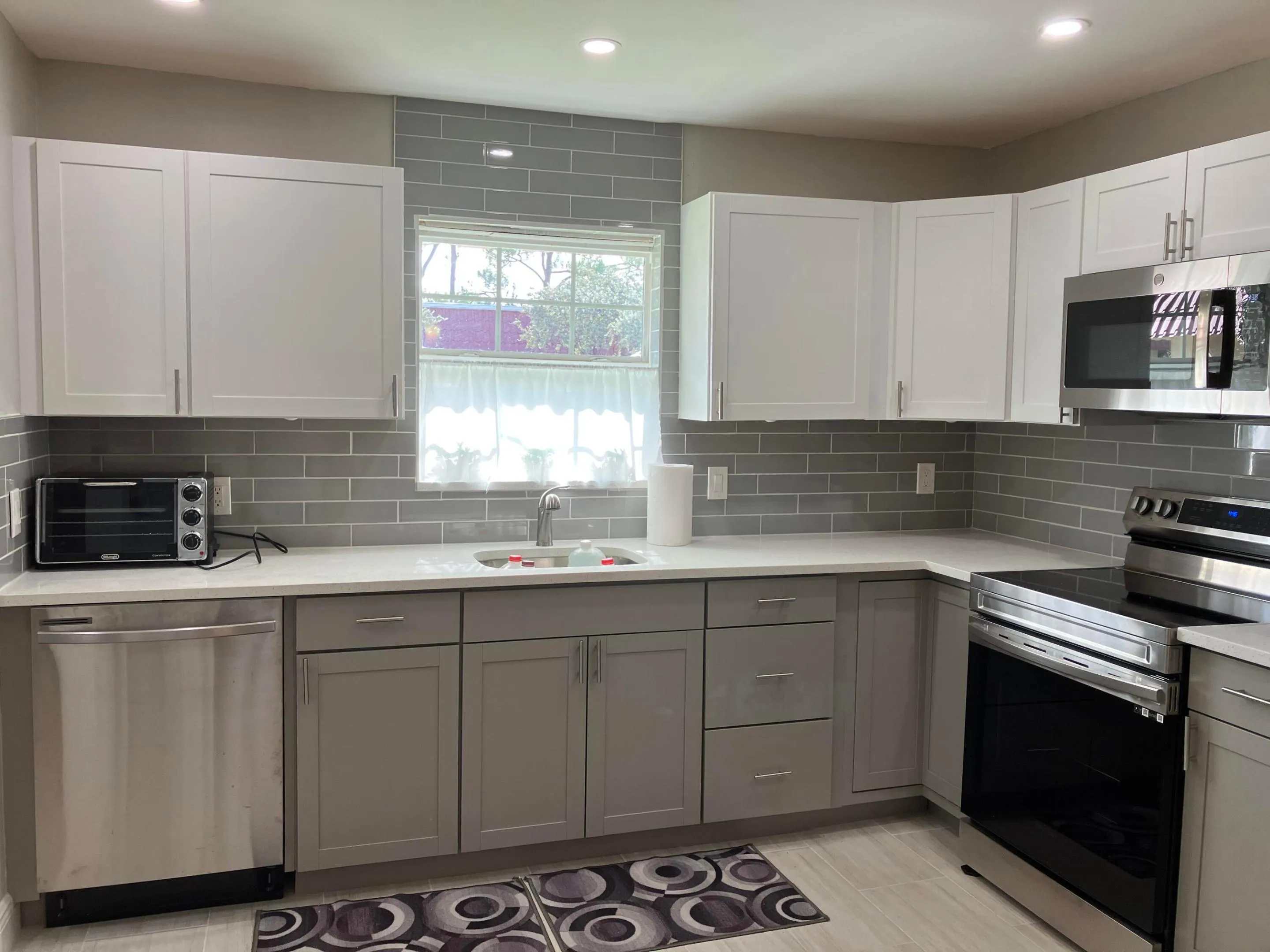 Kitchen featuring stainless steel appliances, a white composite sink, white upper cabinetry, and gray lower cabinetry